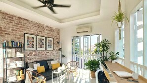 A bright living room with a brick wall, a sofa, a coffee table, and a bookshelf. - Sleepy Nomad Hostel (Malacca City)