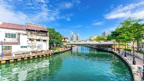 A canal with buildings on either side, a bridge in the background, and a clear sky. - Sleepy Nomad Hostel (Malacca City)