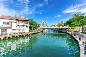 A canal with buildings on either side, a bridge in the background, and a clear sky. - Sleepy Nomad Hostel (Malacca City)