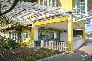 A yellow building with a covered patio area, a wooden deck, and a white railing. - Sleepy Nomad Hostel (Malacca City)