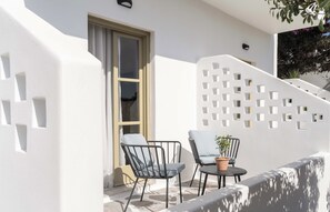 A white exterior wall with a geometric cut-out design, a window, and a small outdoor seating area with two chairs and a table. - Philosophy Of Mykonos (Mykonos)
