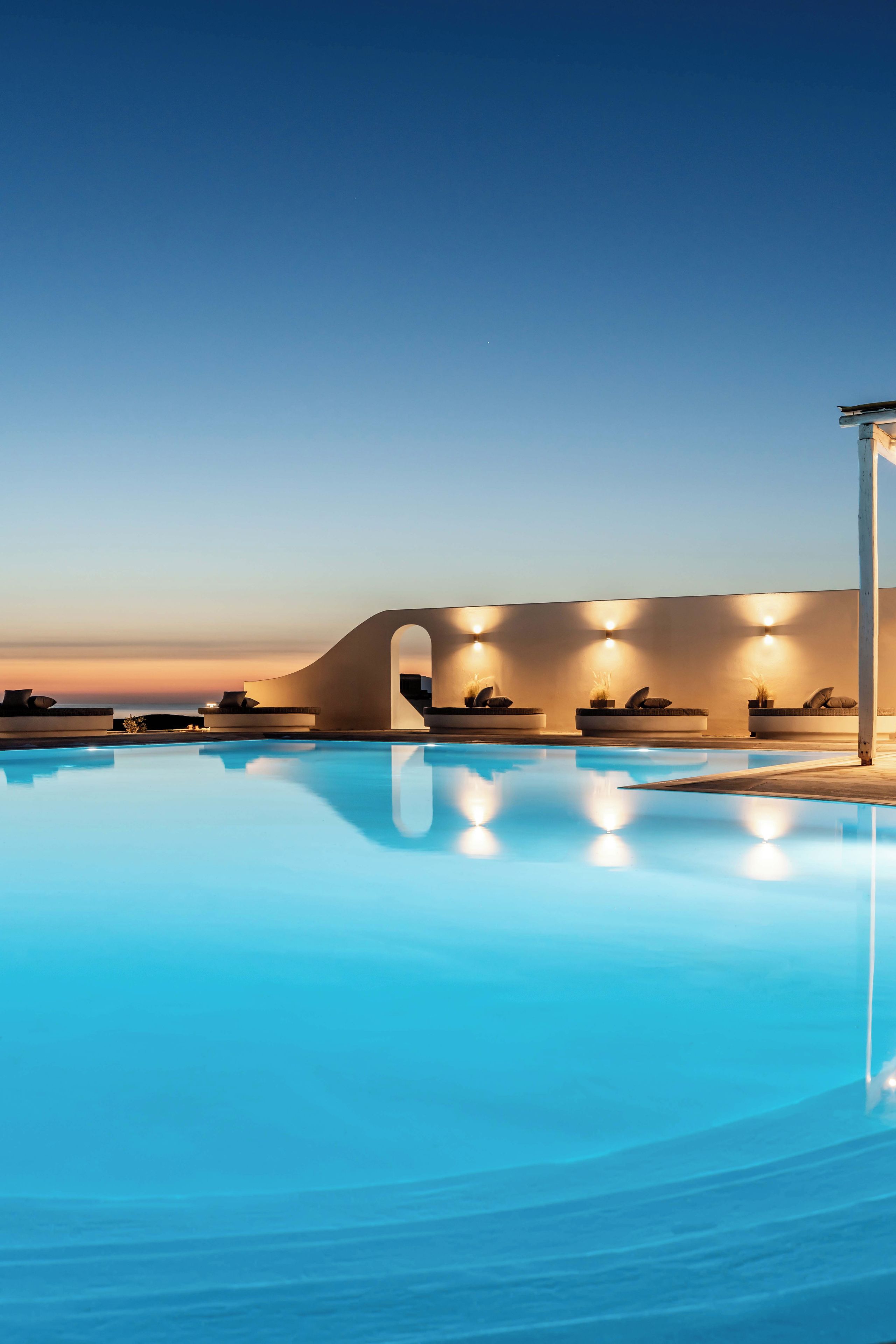 Una piscina con un diseño arquitectónico moderno, que incluye una pared curva y zonas de estar.