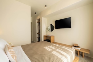 Un dormitorio moderno con una cama grande, un banco de madera, un televisor montado en la pared y un armario con espejo.