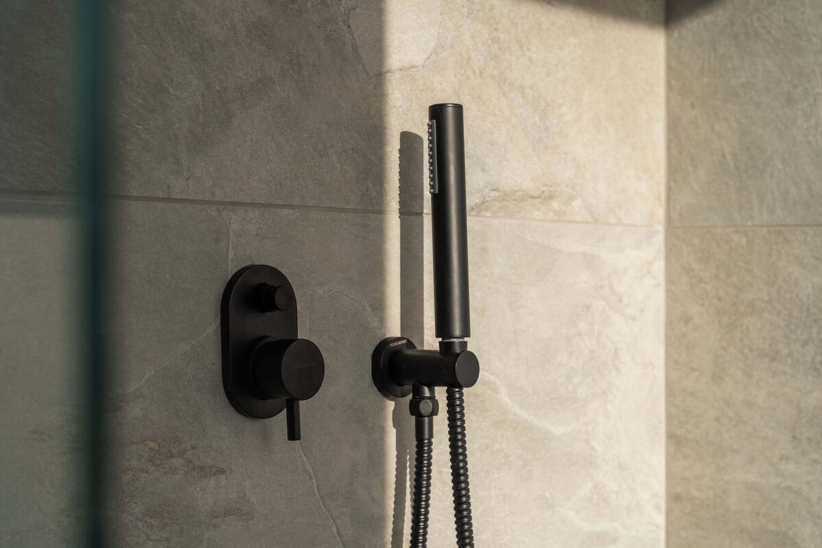 A modern bathroom with a shower head mounted on a wall, a control knob, and a flexible hose.