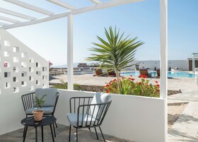 A terrace with two chairs and a table, a pool, and a view of the sea.