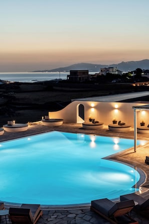 A swimming pool with lounge chairs and a seating area with built-in lighting, overlooking a coastal landscape. - Philosophy Of Mykonos (Mykonos)