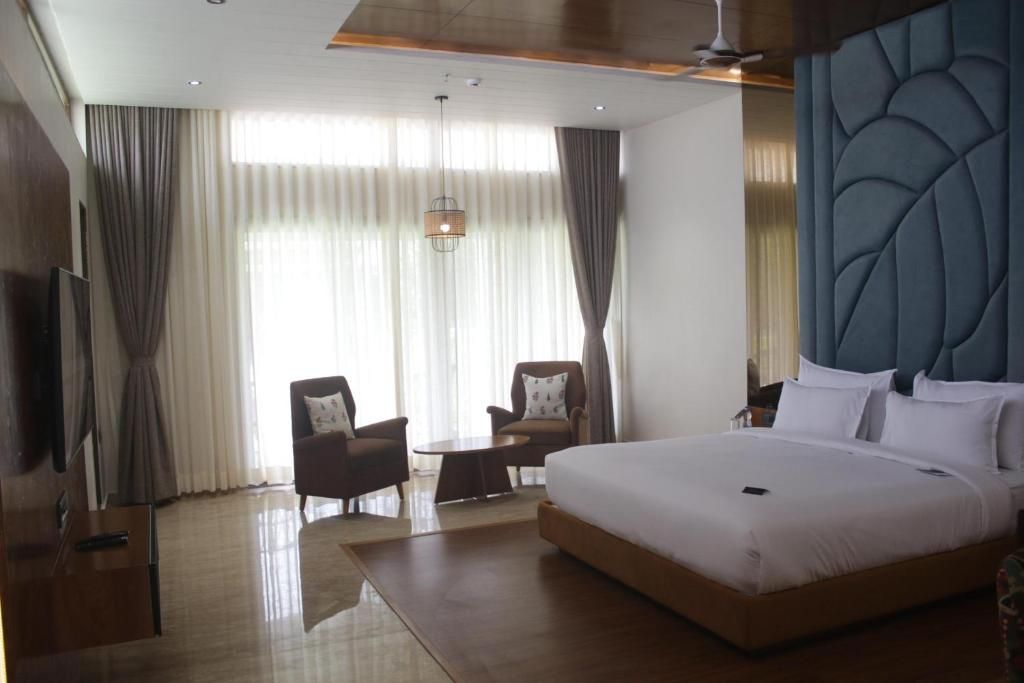 Ein modernes Hotelzimmer mit einem großen Bett, zwei Sesseln, einem kleinen Tisch und einem Fernseher.