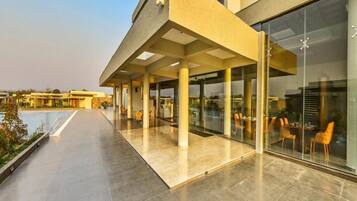 A modern hotel exterior with a covered outdoor seating area, a pool, and large windows.
