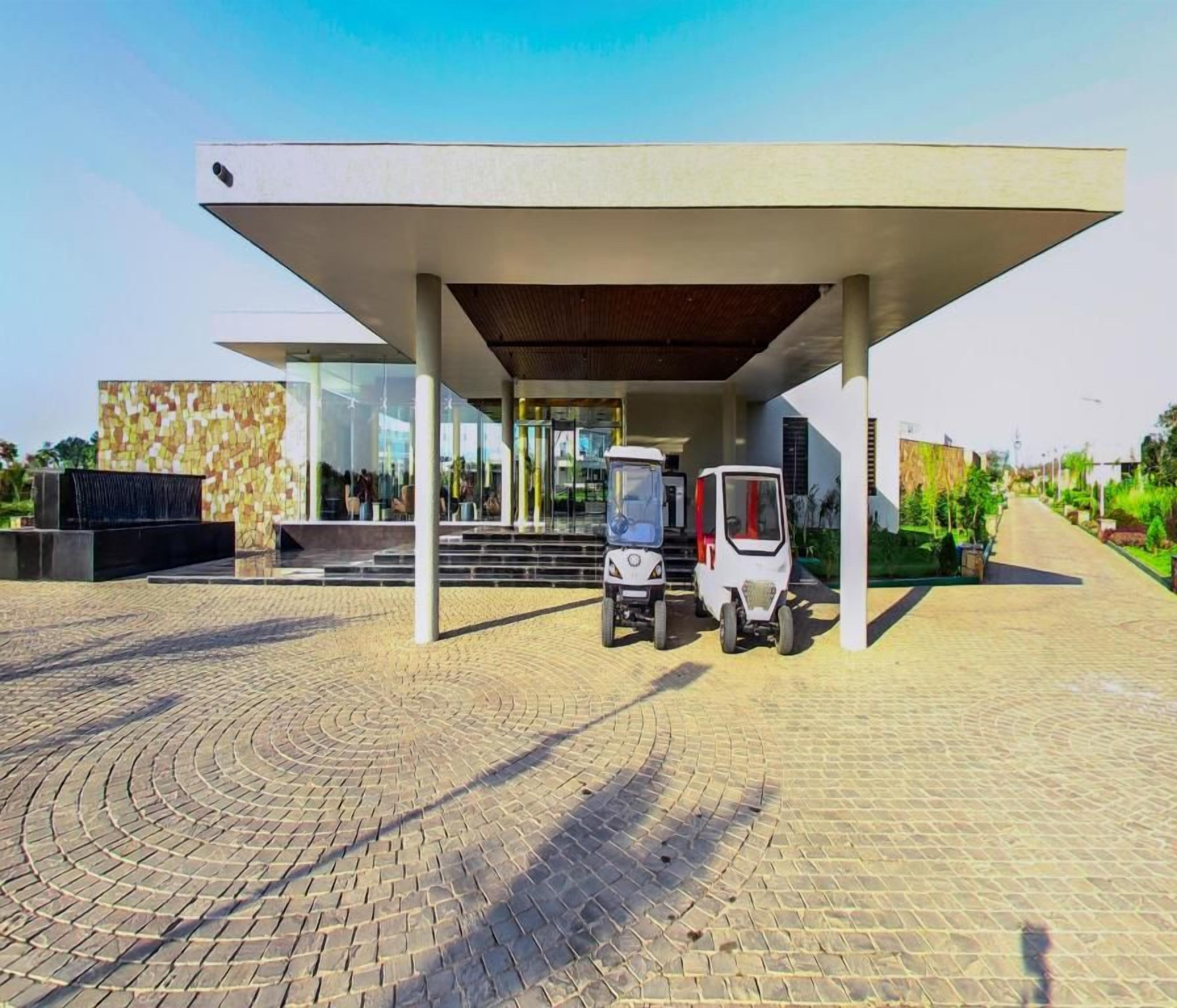 A modern building with a covered entrance, two tricycles parked outside, and a paved area with a circular pattern.
