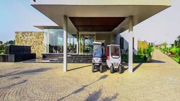 A modern building with a covered entrance, two tricycles parked outside, and a paved area with a circular pattern.