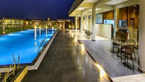 A swimming pool with a view of the night sky, a bar area with seating, and a modern building facade. - Araiya Gir,a Mavintara Resort (Talala)
