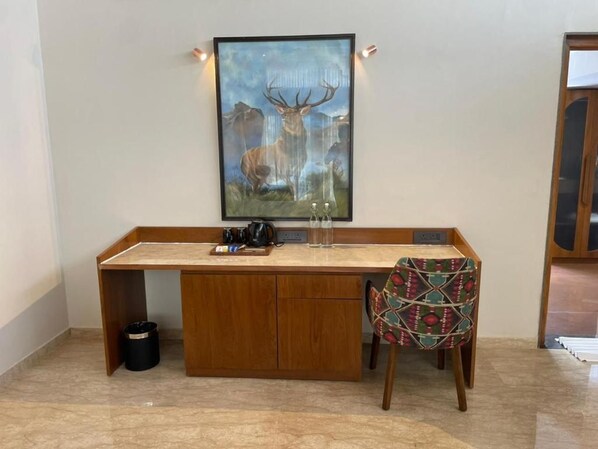 A wooden desk with a framed wildlife painting, a chair with a patterned cushion, and a trash bin. - Araiya Gir,a Mavintara Resort (Talala)
