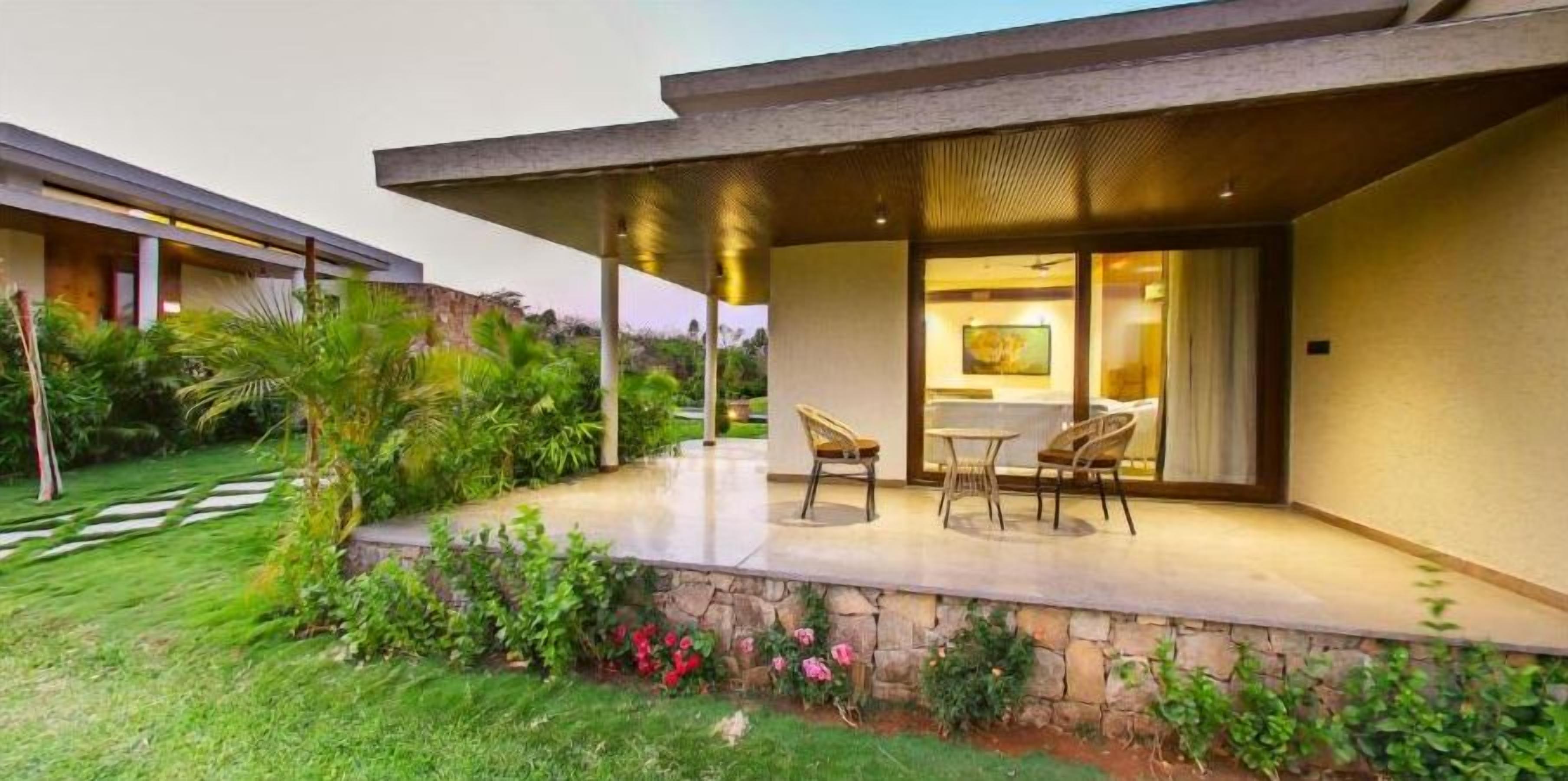 Una casa moderna con patio coperto, muro di sostegno in pietra e giardino rigoglioso.