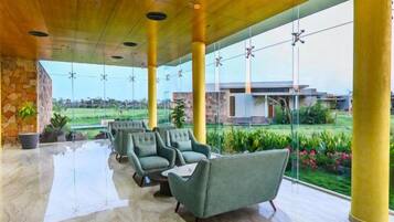 A spacious indoor area with a glass wall offering a view of a garden and a building. There are several chairs arranged for seating.