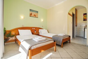 Habitación de hotel con dos camas individuales, cabecera de madera, mesita de noche, lámpara de pared, un cuadro y un baño con azulejos visible a través de un arco.