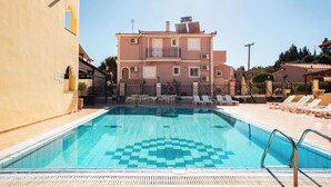 A swimming pool with a tiled deck, lounge chairs, and a building with a balcony in the background. - Solena Studios Kavos (Corfu)