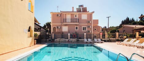 A swimming pool with a tiled deck, lounge chairs, and a building with a balcony in the background.