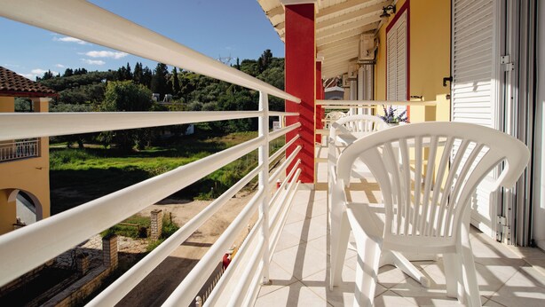 A balcony with white railings, a red pillar, and a view of a green landscape. - Solena Studios Kavos (Corfu)