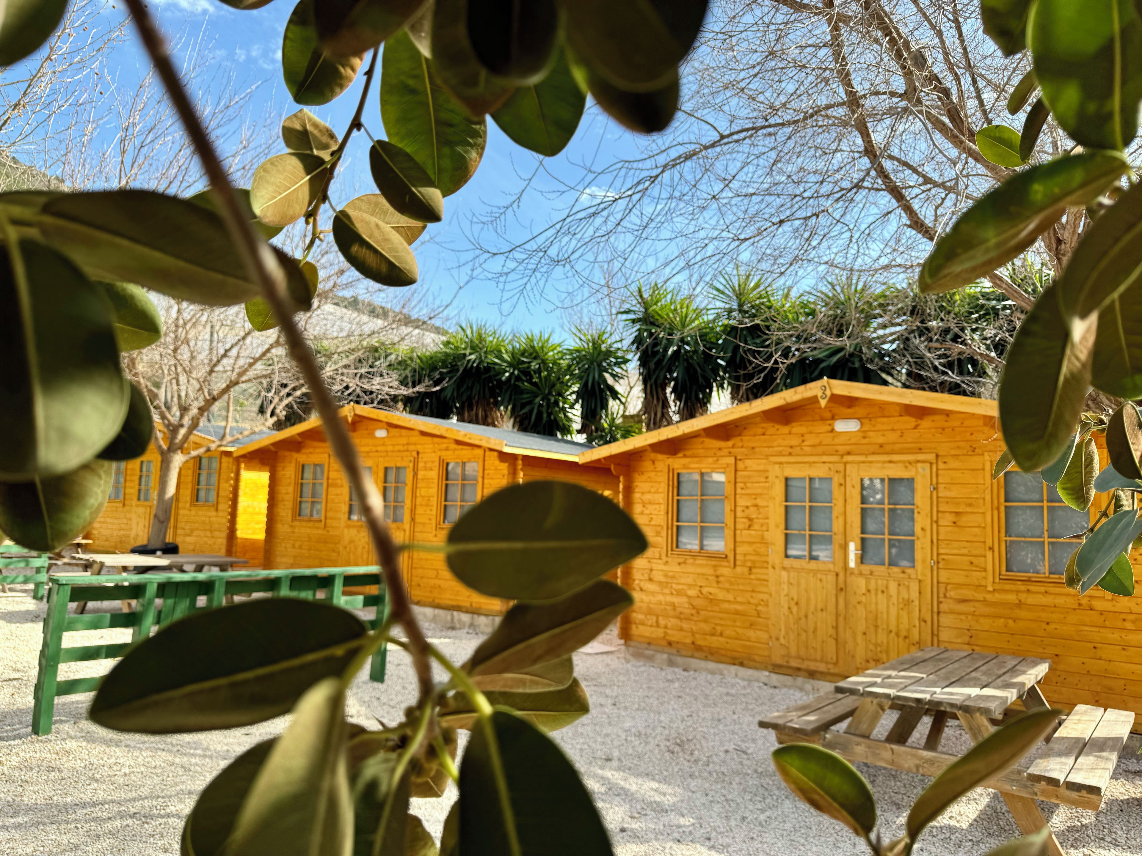 Una cabaña de madera con suelo de grava, una mesa de madera y un banco.