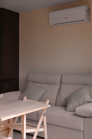 A room with a grey sofa, a wooden table, and an air conditioning unit mounted on the wall. - Bike Camp Algar Costa Blanca (Callosa d' En Sarria)