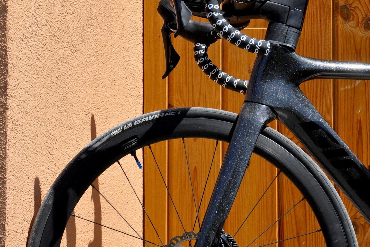 Una bicicleta con cuadro y asiento negros, apoyada contra una cerca de madera con un muro anaranjado con textura.