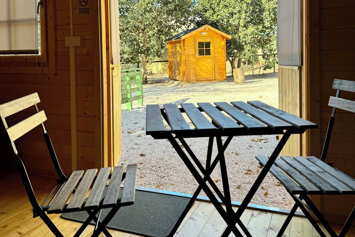 A wooden cabin with a picnic table and chairs in front of a door leading outside.