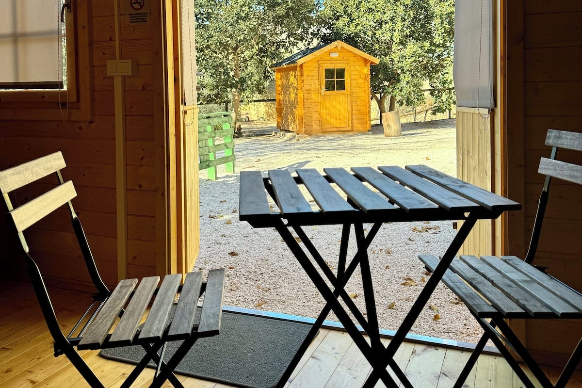 A wooden cabin with a picnic table and chairs in front of a door leading outside.