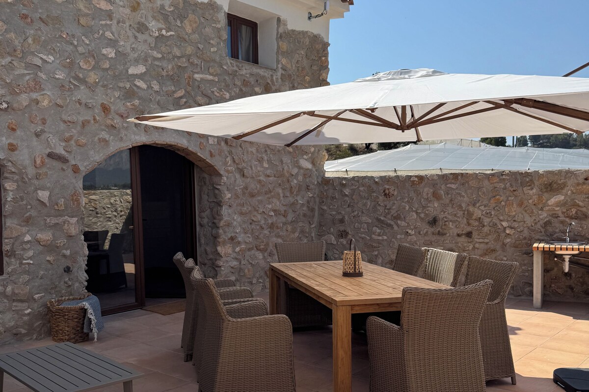 A stone building with a tiled patio, outdoor furniture, and umbrellas.