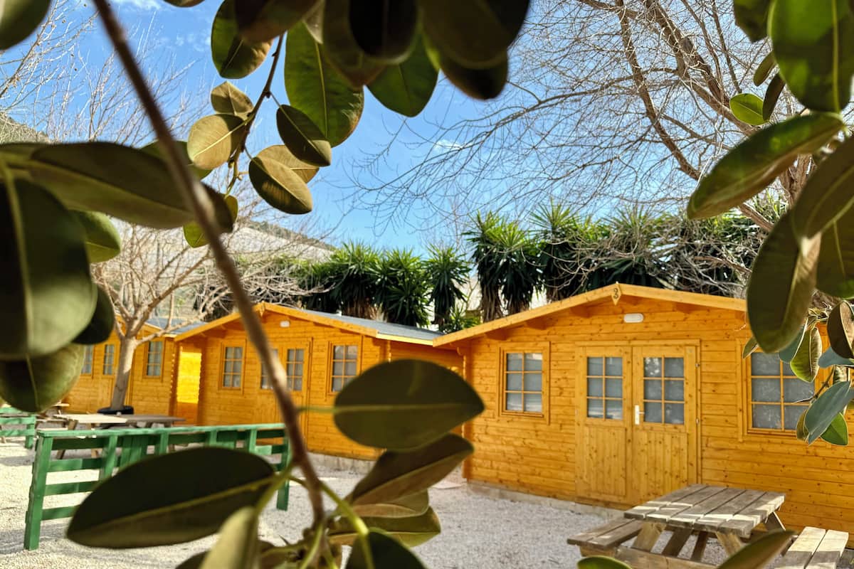 Una cabaña de madera con suelo de grava, una mesa de madera y un banco.