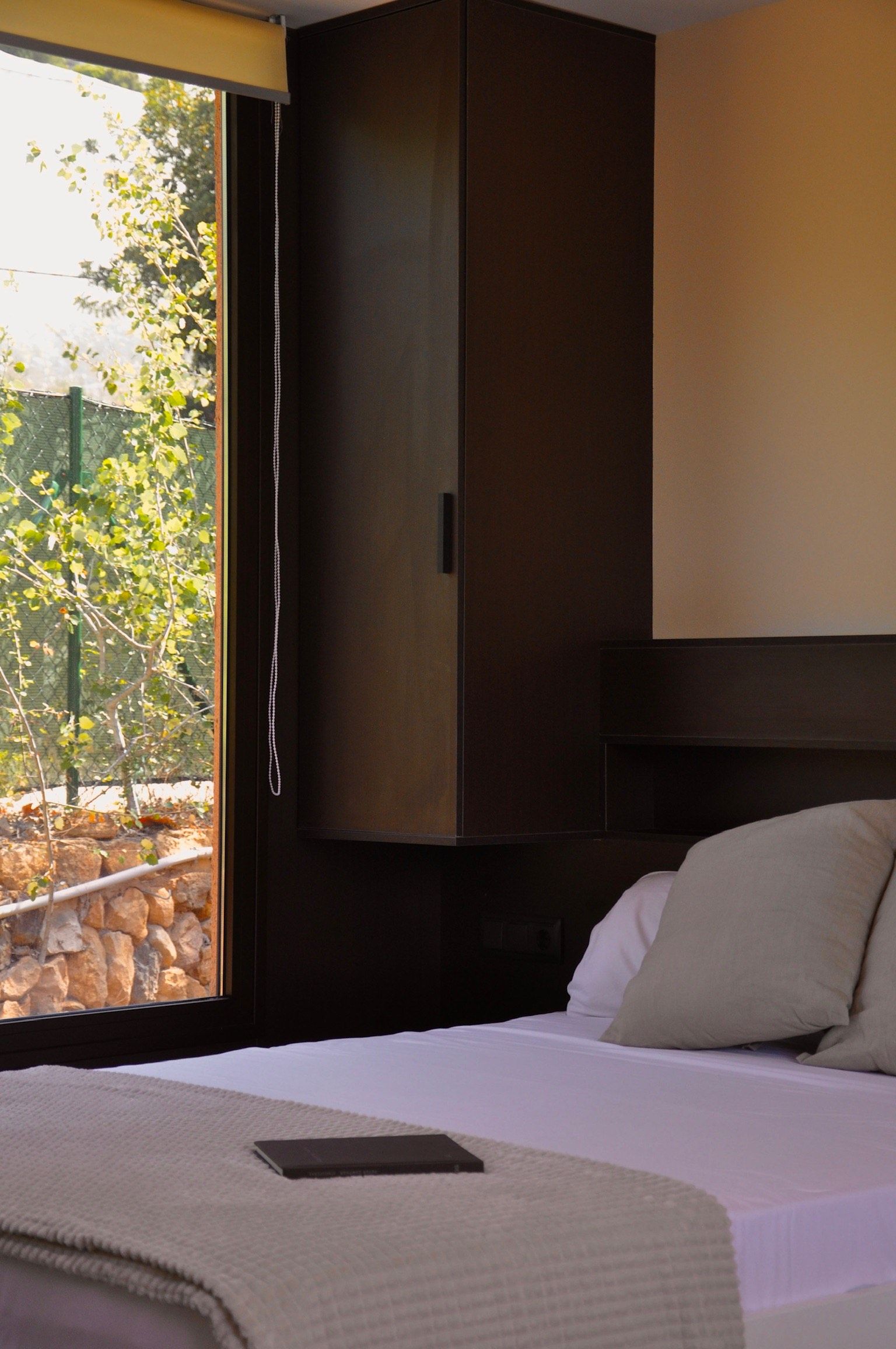 Un dormitorio con cama, ventana con vista a árboles y un armario de color oscuro.