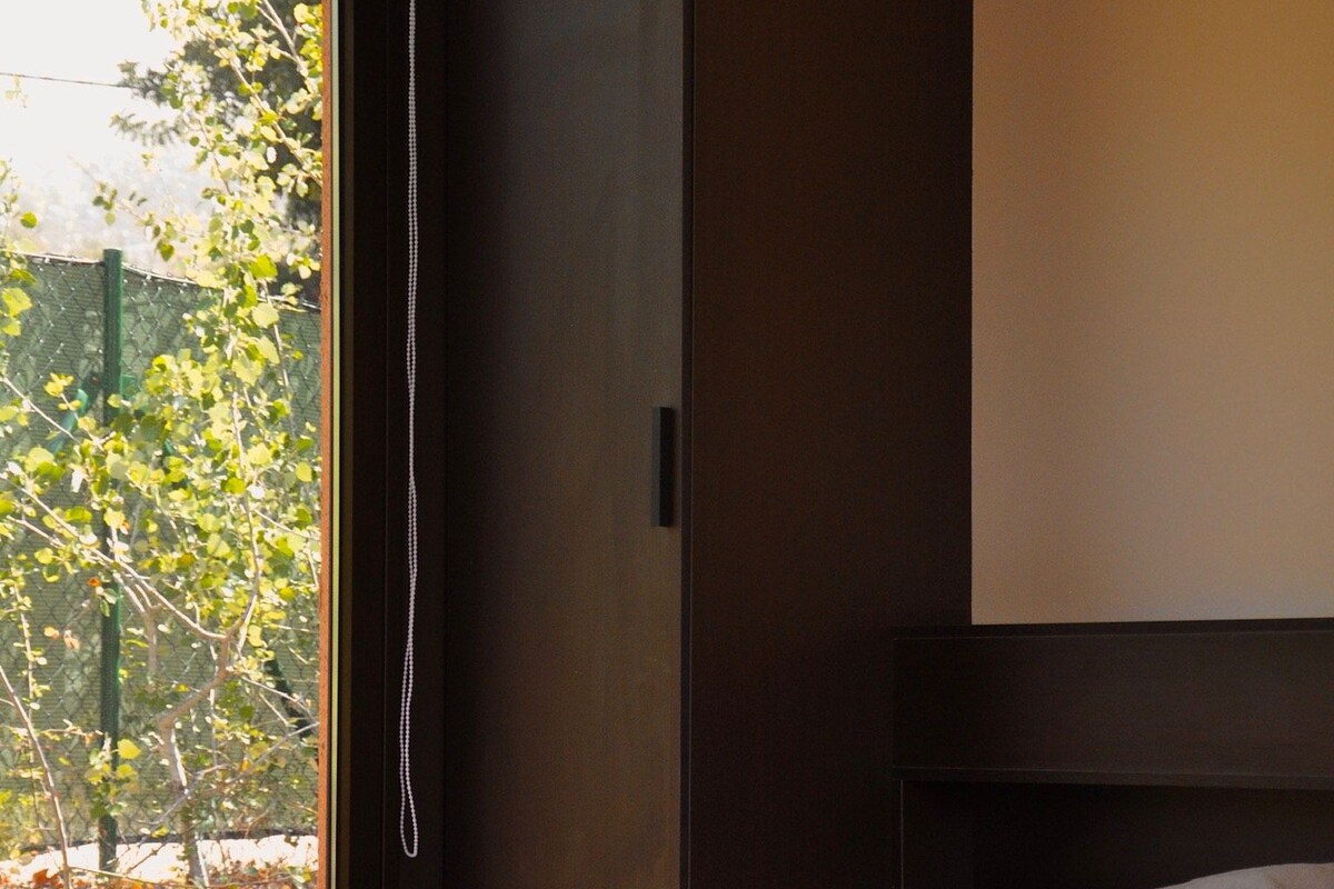 A bedroom with a bed, a window with a view of trees, and a dark-colored wardrobe.