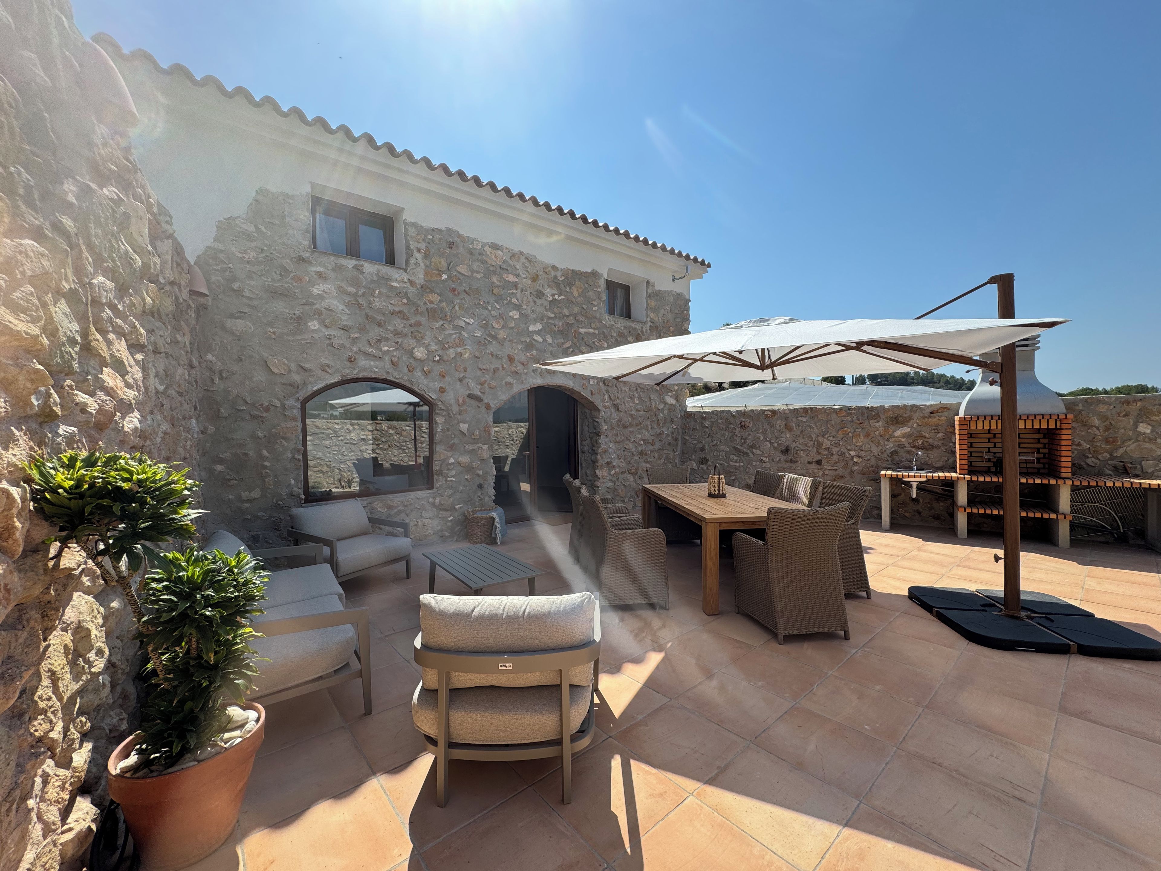Edificio de piedra con un patio que cuenta con mobiliario exterior, una parrilla y plantas en macetas.