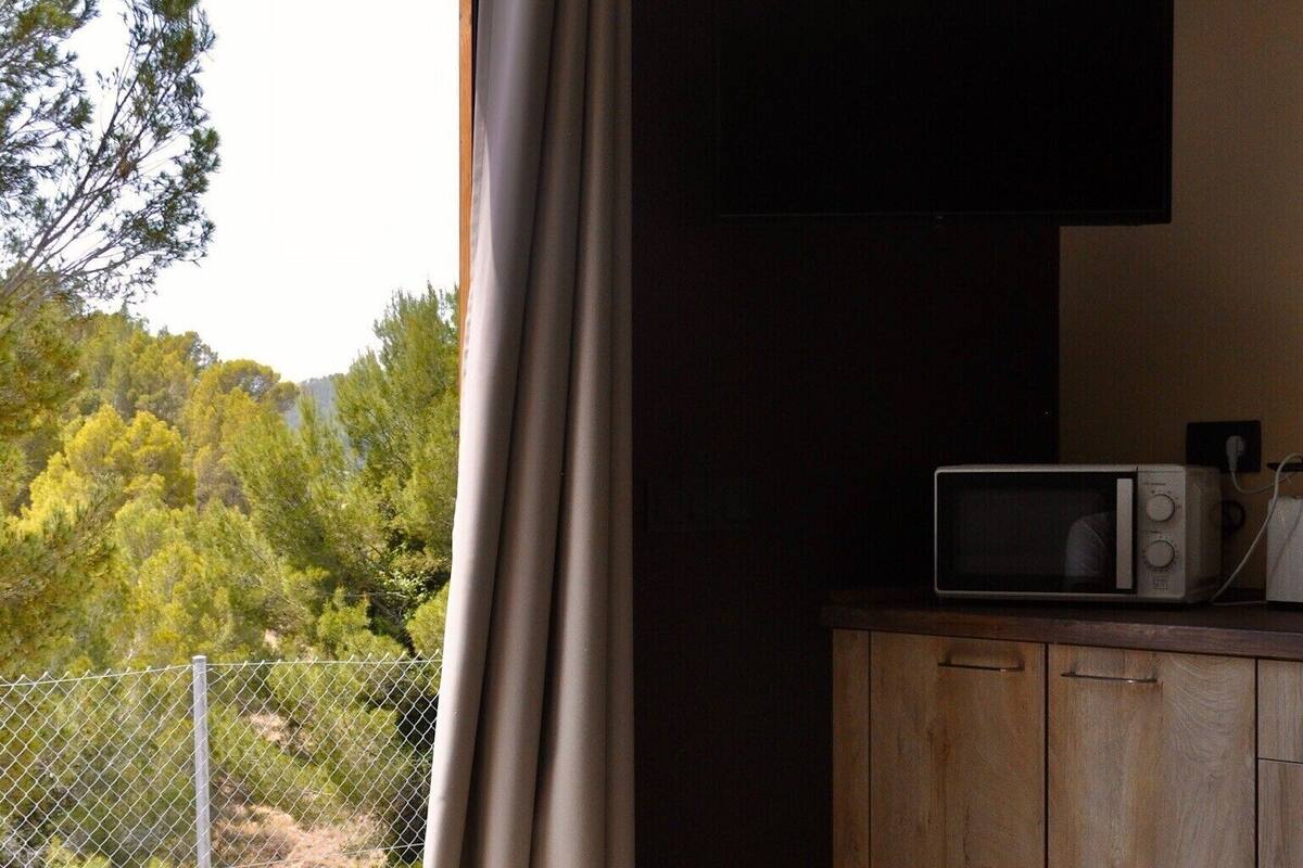 A room with a large sliding glass door, a microwave on a wooden cabinet, and a view of trees and hills outside.