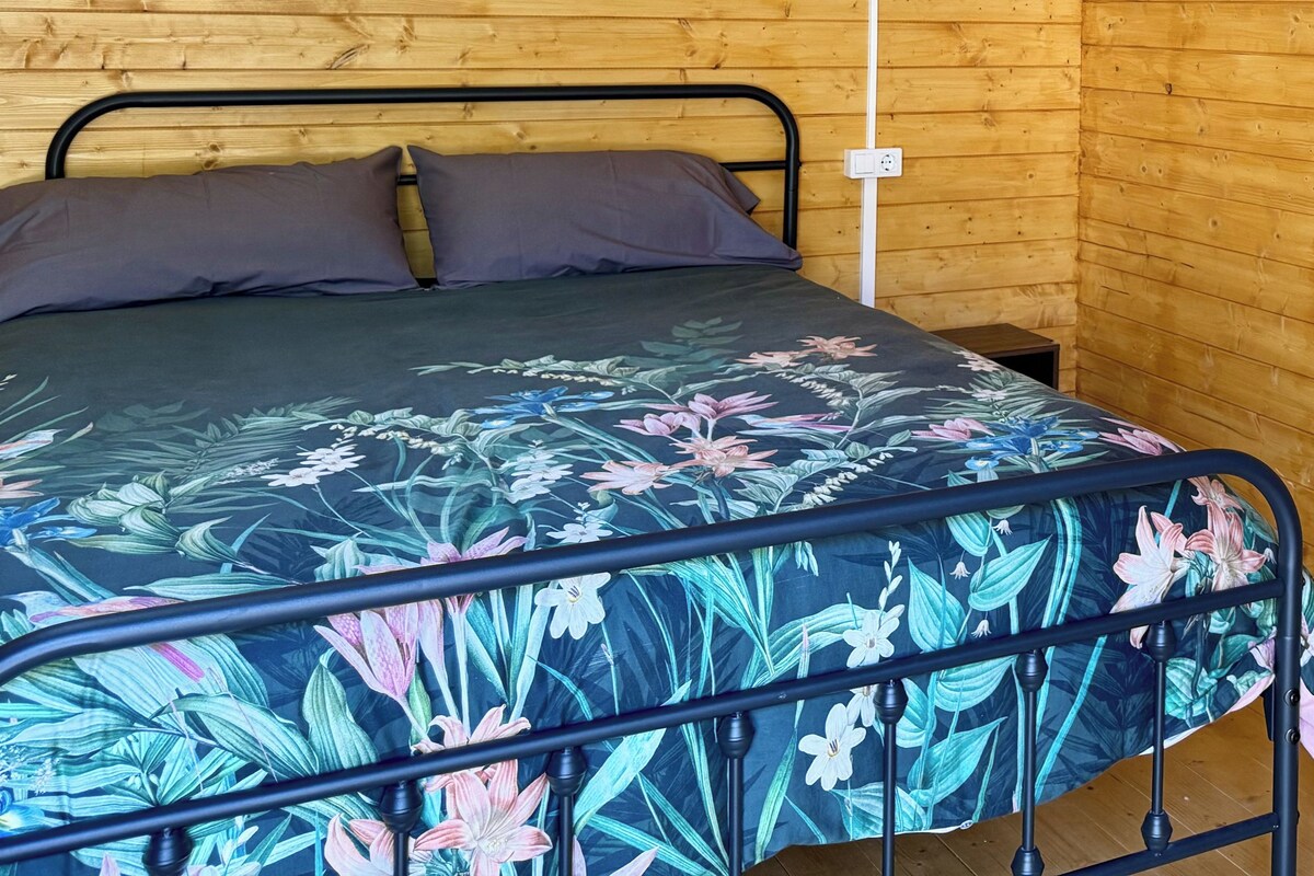 Una habitación de cabaña de madera con una cama, una lámpara en la pared y un estante con una toalla.