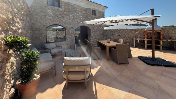 Ein Steinhaus mit einer Terrasse, die Gartenmöbel, einen Grill und Kübelpflanzen bietet.