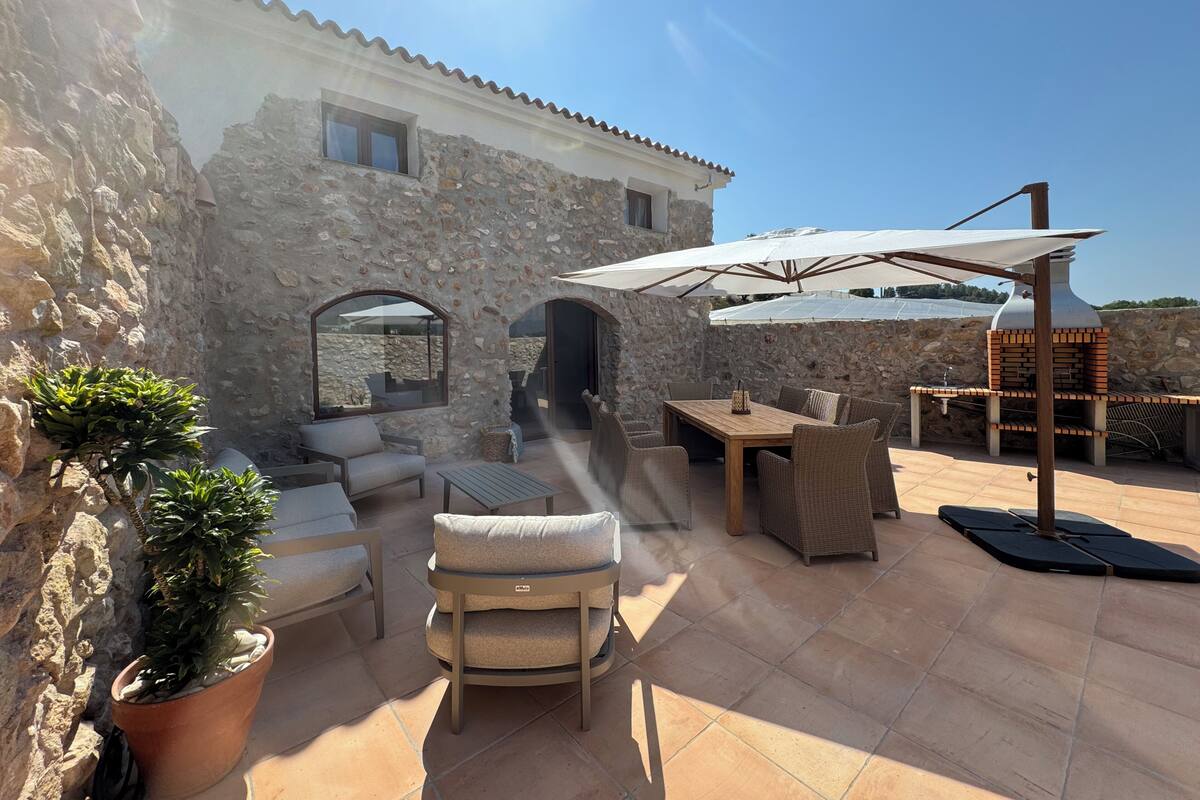 A stone building with a patio area featuring outdoor furniture, a grill, and potted plants.