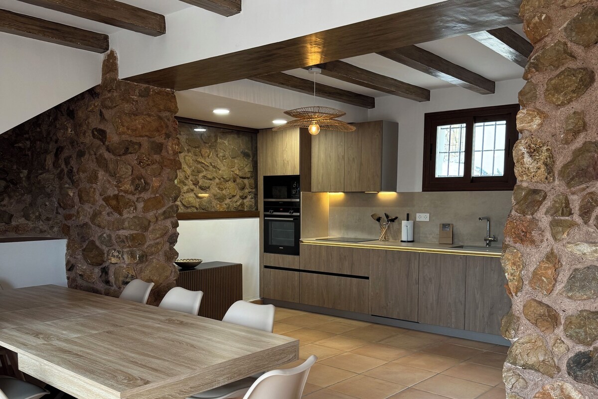 Una cocina moderna con paredes de piedra, vigas de madera y un comedor con una mesa grande y sillas.