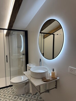 Un baño moderno con ducha de vidrio, lavabo blanco y un espejo grande.