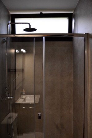 Un baño moderno con ducha envuelta en vidrio, lavamanos a la vista y ventana sobre la ducha.