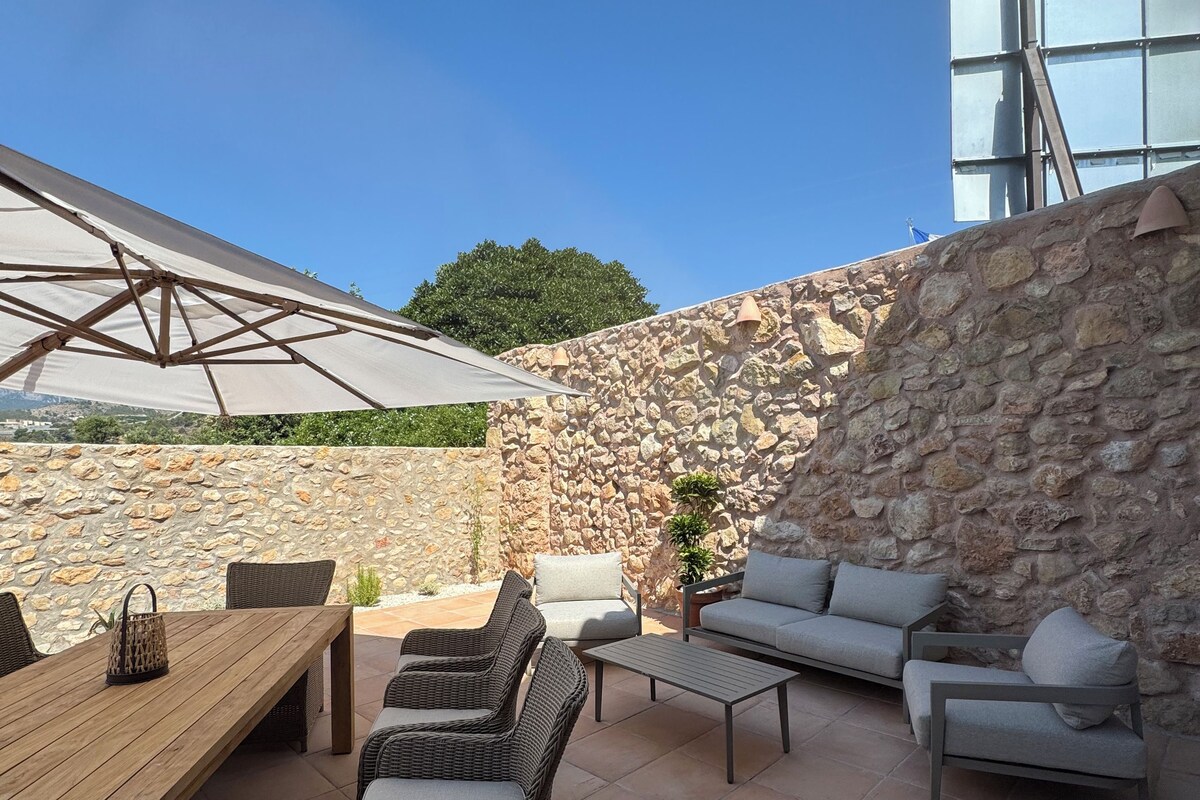 Un patio al aire libre con pared de piedra, mobiliario de mimbre, una mesa de madera y un paraguas grande.