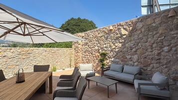 Un patio al aire libre con pared de piedra, mobiliario de mimbre, una mesa de madera y un paraguas grande.