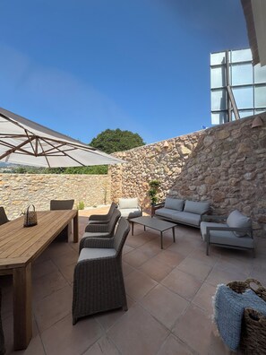 Un patio al aire libre con pared de piedra, mobiliario de mimbre, una mesa de madera y un paraguas grande.