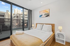 A modern hotel room with a large bed, a city view through floor-to-ceiling windows, a painting on the wall, and a small bedside table with a lamp. - Modern 3BR Apartment in Sunnybank |Pool&Gym Access (South Brisbane)
