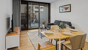 Una sala de estar moderna con comedor, un sofá, un televisor y un ventanal que da a un espacio exterior.