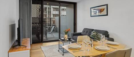 A modern living room with a dining area, a sofa, a TV, and a sliding glass door leading to an outdoor space.