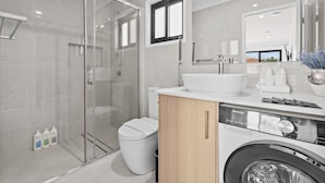 Une salle de bain moderne avec une douche à parois de verre, un lavabo blanc et un lave-linge encastré.