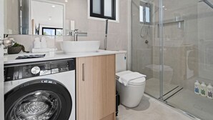 Ein modernes Badezimmer mit Waschmaschine, großem Waschbecken und einer Duschkabine.