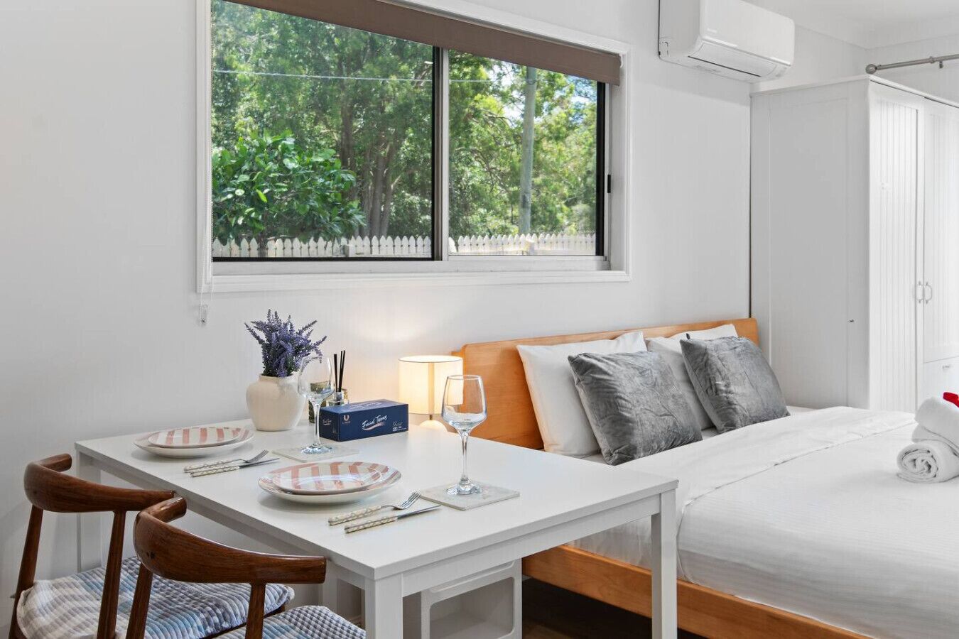 Une chambre bien rangée, avec un lit, une table de chevet et une fenêtre donnant sur un paysage verdoyant.