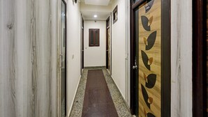 Un couloir aux murs de marbre, une porte en bois ornée d’un motif de feuilles et une fenêtre avec un cadre en bois.