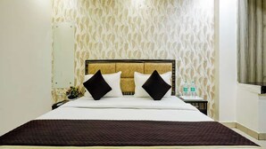 A hotel room with a large bed, two pillows, a nightstand, a plant, and a window with curtains. - Hotel Lookout Stay (New Delhi)